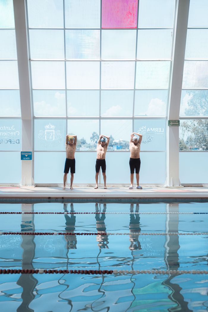 Three men exercising by the indoor swimming pool, preparing for swimming practice.