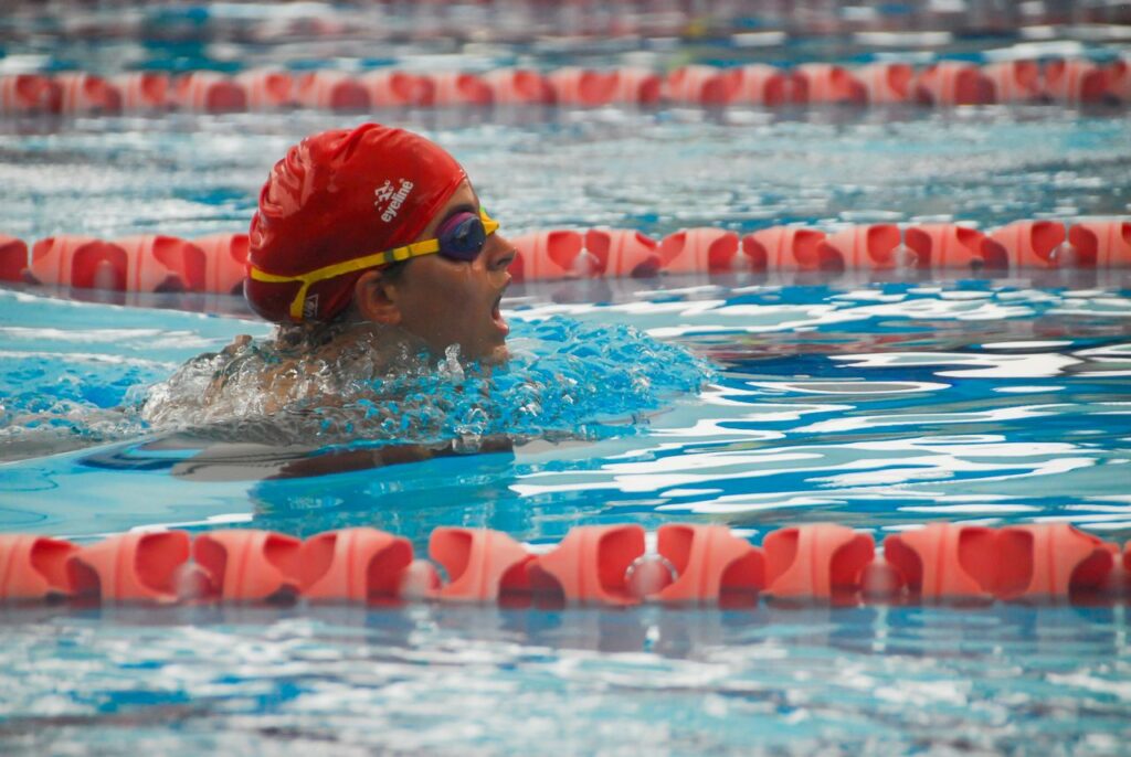 Swimmer with goggles and cap in a swimming pool during a breaststroke race.