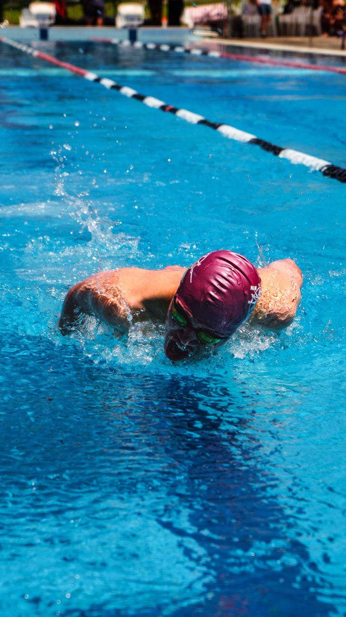 Swimmer in a blue pool performing freestyle stroke during daytime competition.