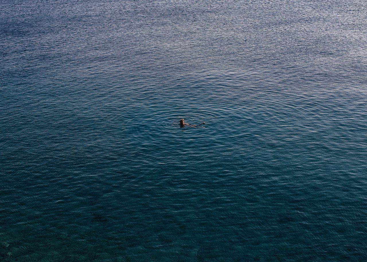 A lone swimmer enjoys a peaceful moment in the vast turquoise ocean, seen from above.