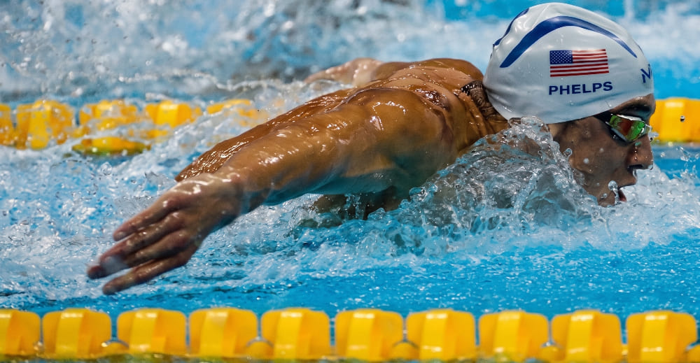 Michael Phelps ejecutando con máxima potencia la brazada de mariposa durante una sesión en piscina olímpica.