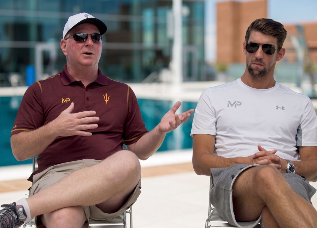 El entrenador Bob Bowman conversando junto a la piscina con el nadador olímpico Michael Phelps sobre su método y planificación deportiva.