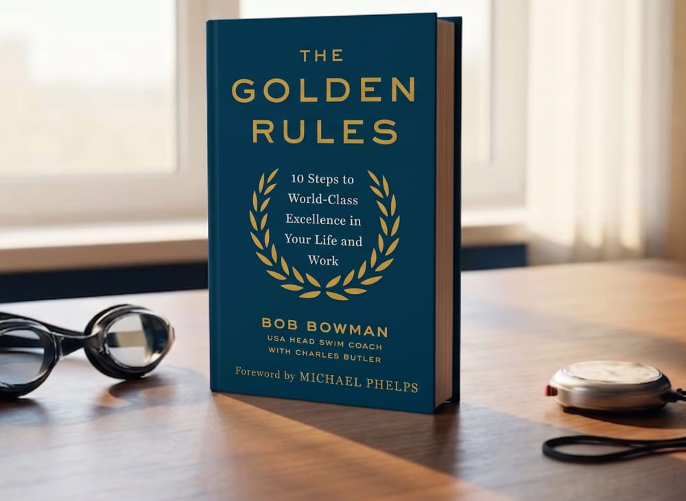 Edición en tapa dura del libro The Golden Rules de Bob Bowman sobre una mesa con gafas de natación y cronómetro