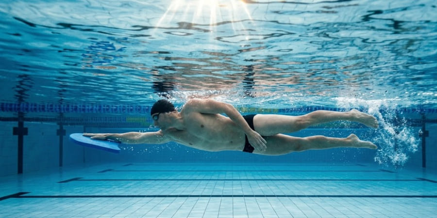 nadador ejecutando el ejercicio de patada lateral con tabla en la alberca, manteniendo el brazo inferior extendido, el cuerpo de costado y las caderas elevadas para perfeccionar la rotación y la alineación corporal en natación.
