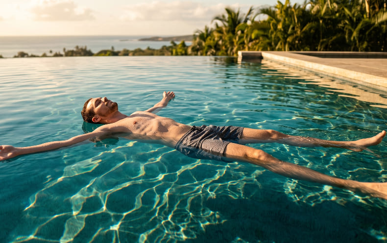 Una fotografía panorámica ultra realista y de alto impacto de un hombre flotando plácidamente boca arriba en una piscina de agua turquesa cristalina.